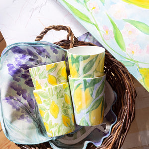 Muggar från serien ‘Citrons de Provence’ av Lena Linderholm – fyra olika citronmotiv i färgstarka pasteller, liggande i en korg med målning i bakgrunden