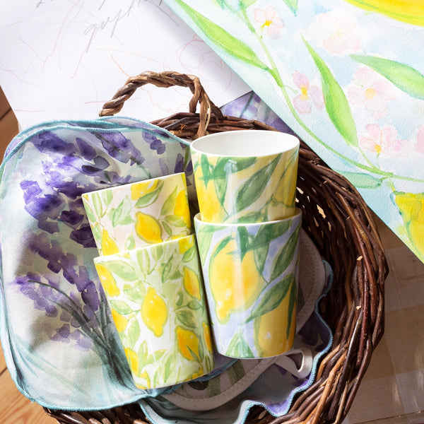 Muggar från serien ‘Citrons de Provence’ av Lena Linderholm – fyra olika citronmotiv i färgstarka pasteller, liggande i en korg med målning i bakgrunden