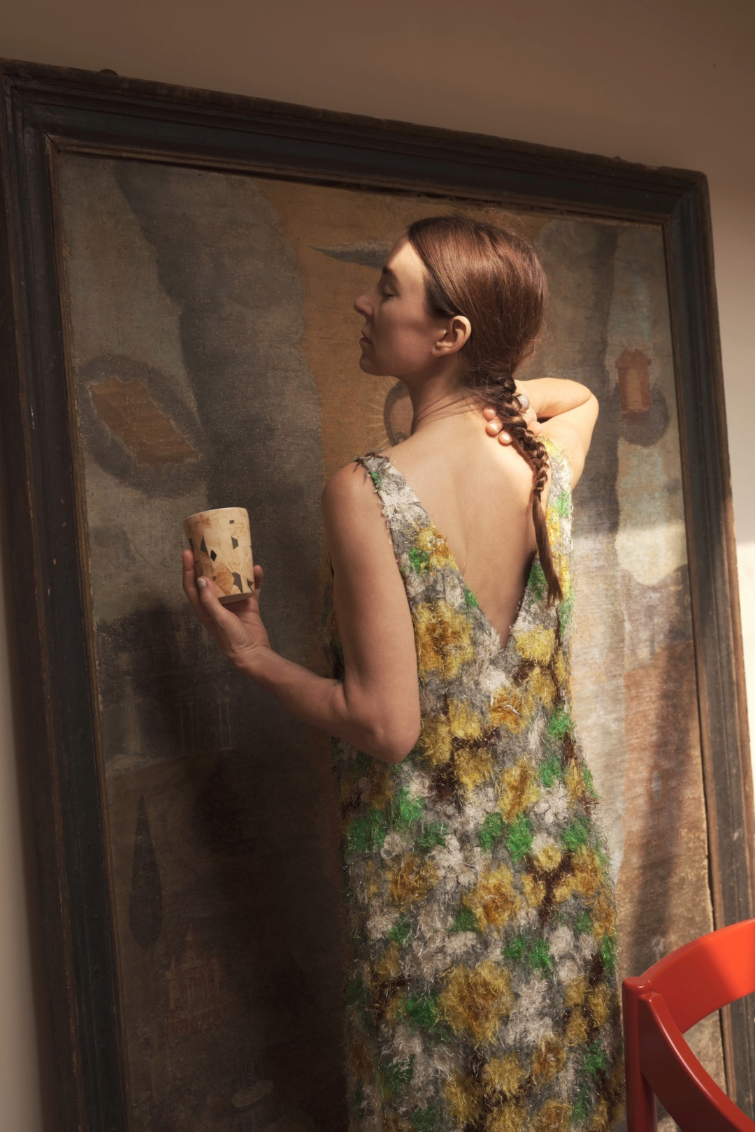 Marie Olsson Nylander i profil, med ryggen mot kameran, håller designmugg Bruno i en elegant pose och klänning.