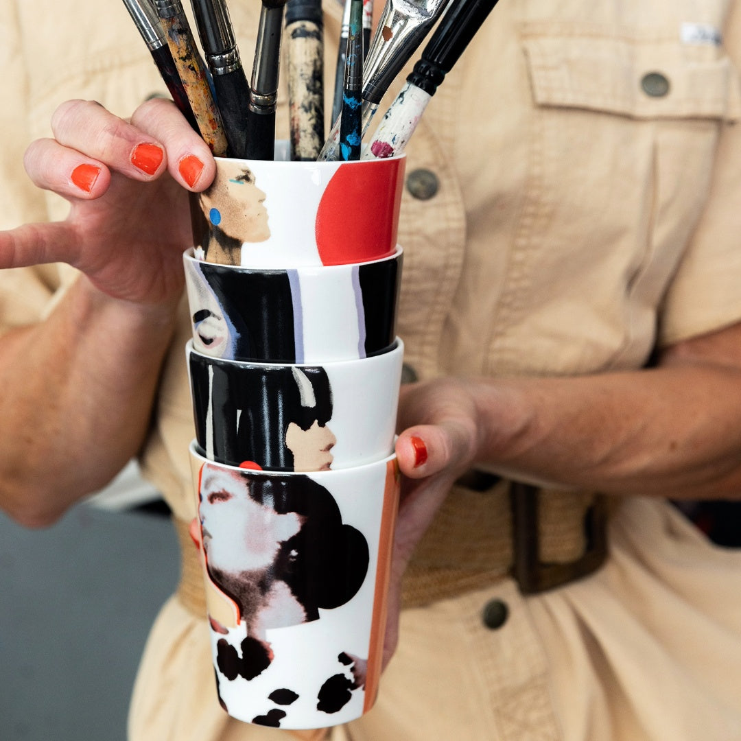 Stina Persson ICONCUPS designmuggar Sisters – staplade benporslinsmuggar med färgstarka akvarellmotiv, översta fylld med penslar.