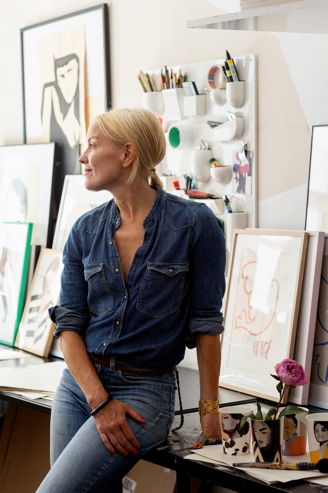 Stina Persson i sin ateljé, lutad mot arbetsbordet med ICONCUPS muggar i bild.