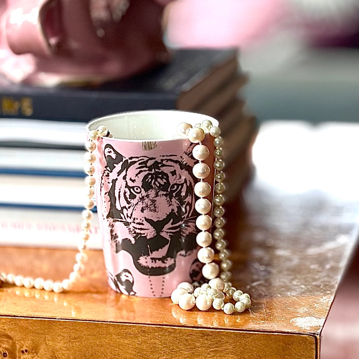 Ljusrosa mugg från serien ‘Coco-Tiger’ av Lisa Bengtsson – tiger­motiv med pärlhalsband som hänger ur, stående på träbord