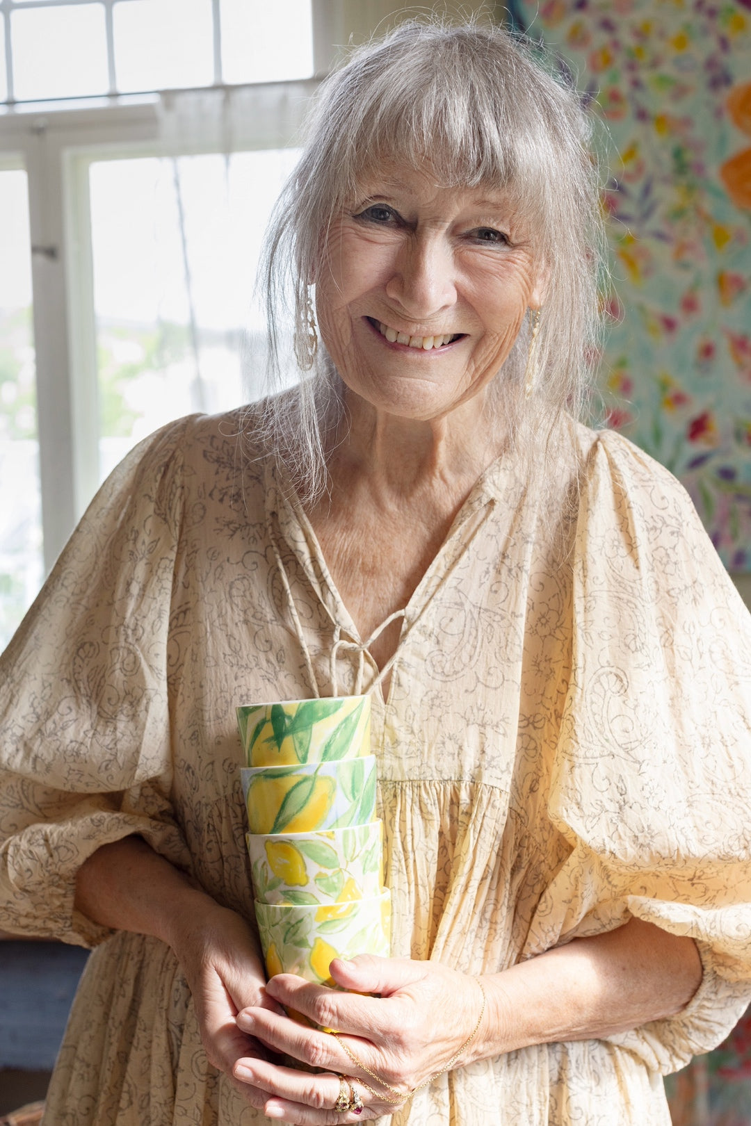 Lena Linderholm i sitt hem, hållande hela kollektionen benporslinsmuggar ur serien Citrons de Provence för ICONCUPS – färgstarka designmuggar med citronmotiv.