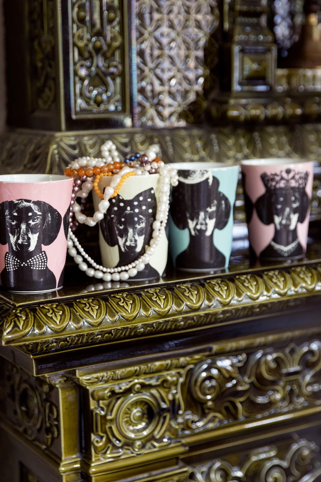 Kollektionen Tillsammans av Studio Lisa Bengtsson – fyra designmuggar med hundmotiv i hattar och flugor, uppställda på en mörkgrön spiselkrans. ICONCUPS